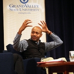 DJ Spooky aka Paul D. Miller with hands raised as if he were putting on a helmet